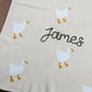 Beige blanket with white ducks and the name 'James'