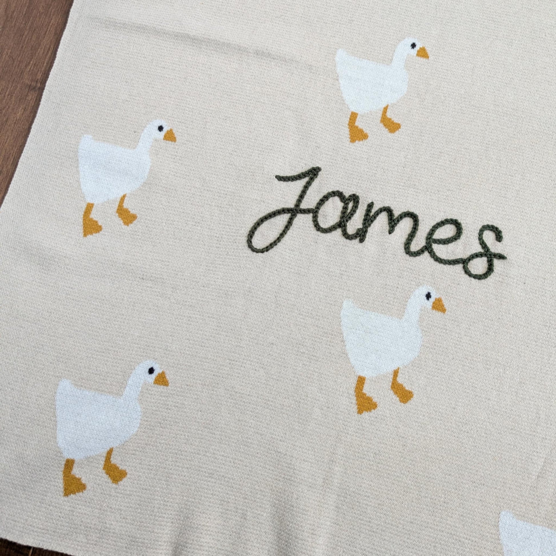 Beige blanket with white ducks and the name 'James'